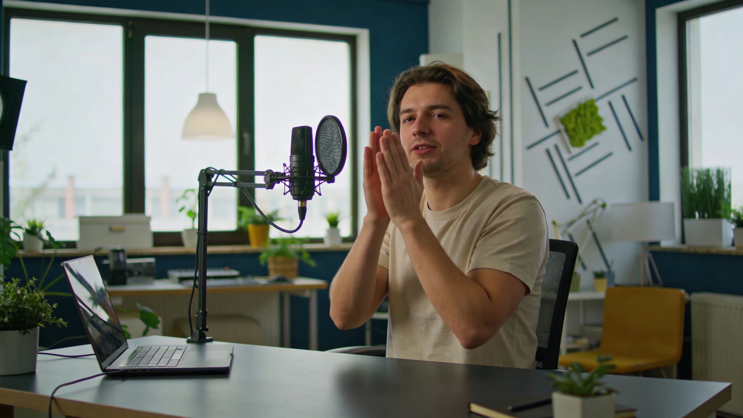 A man gesturing with his hands while sitting at a desk with a studio microphone for podcasting.